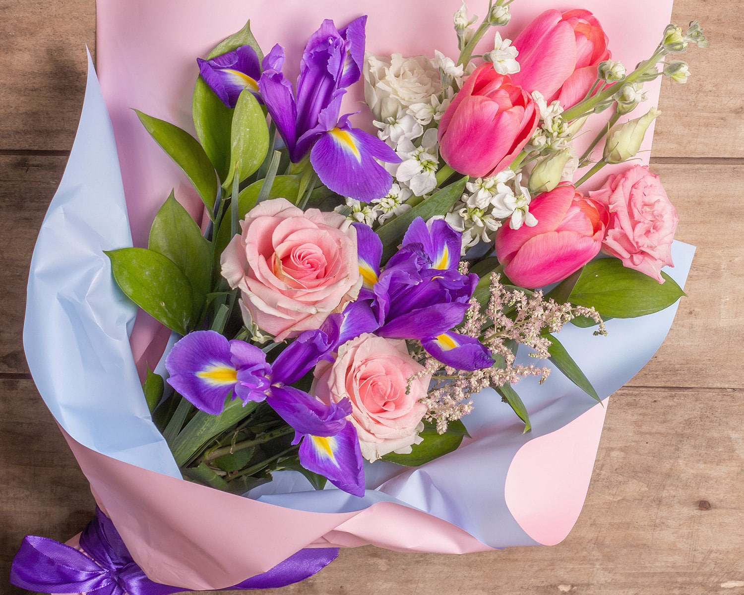 A fresh bouquet of soft pinks, whites and purples, gently laid upon a wooden table